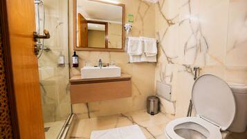 A bathroom with a marble floor, a sink with a mirror above it, a toilet, and a shower area.