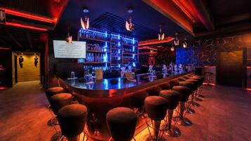Een bar met een lange toonbank, meerdere krukken en een wand vol drankflessen.