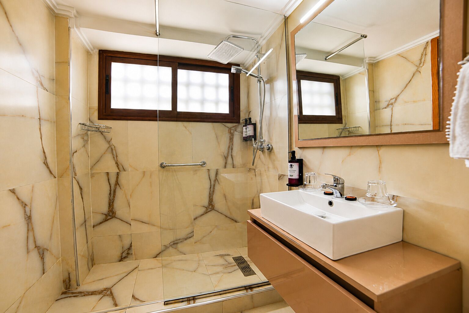 A bathroom with a marble shower, a sink with a mirror, and a window.