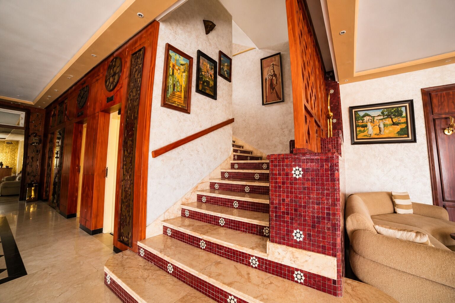 Un magnifique escalier avec des marches recouvertes de carreaux rouges et des rampes en bois, menant à un salon doté d’un canapé beige.