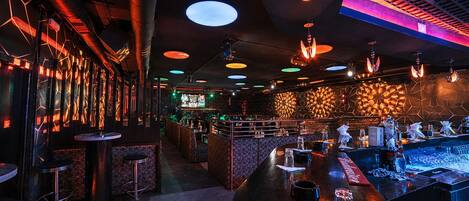 A bar area with round tables, stools, and a counter with bar tools.