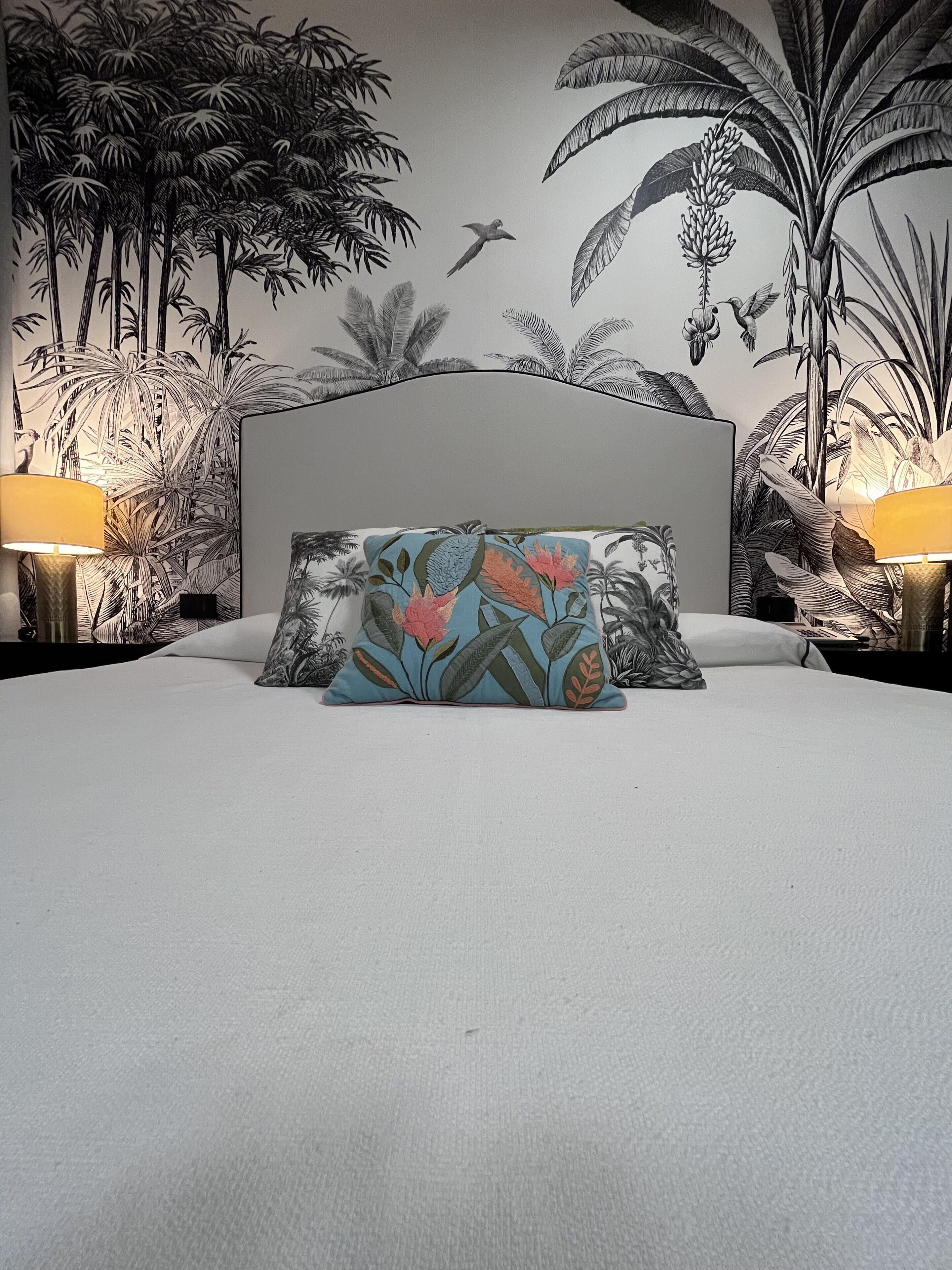 Un lit avec une tête de lit, deux tables de chevet et un mur orné d’une fresque aux motifs tropicaux.