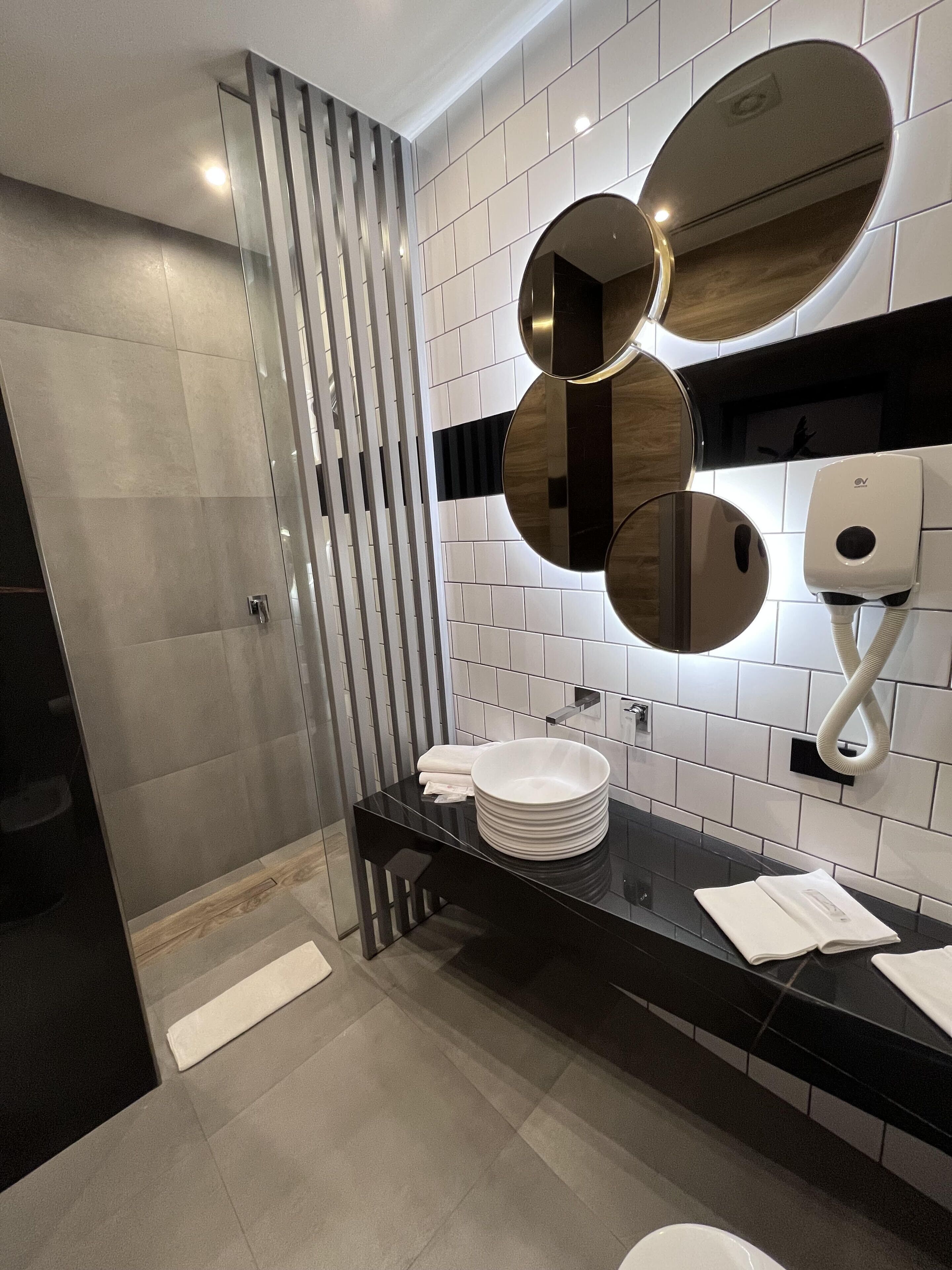 Ein modernes Badezimmer mit schwarzem Waschtisch, weißen Fliesen und einer Glasabtrennung.