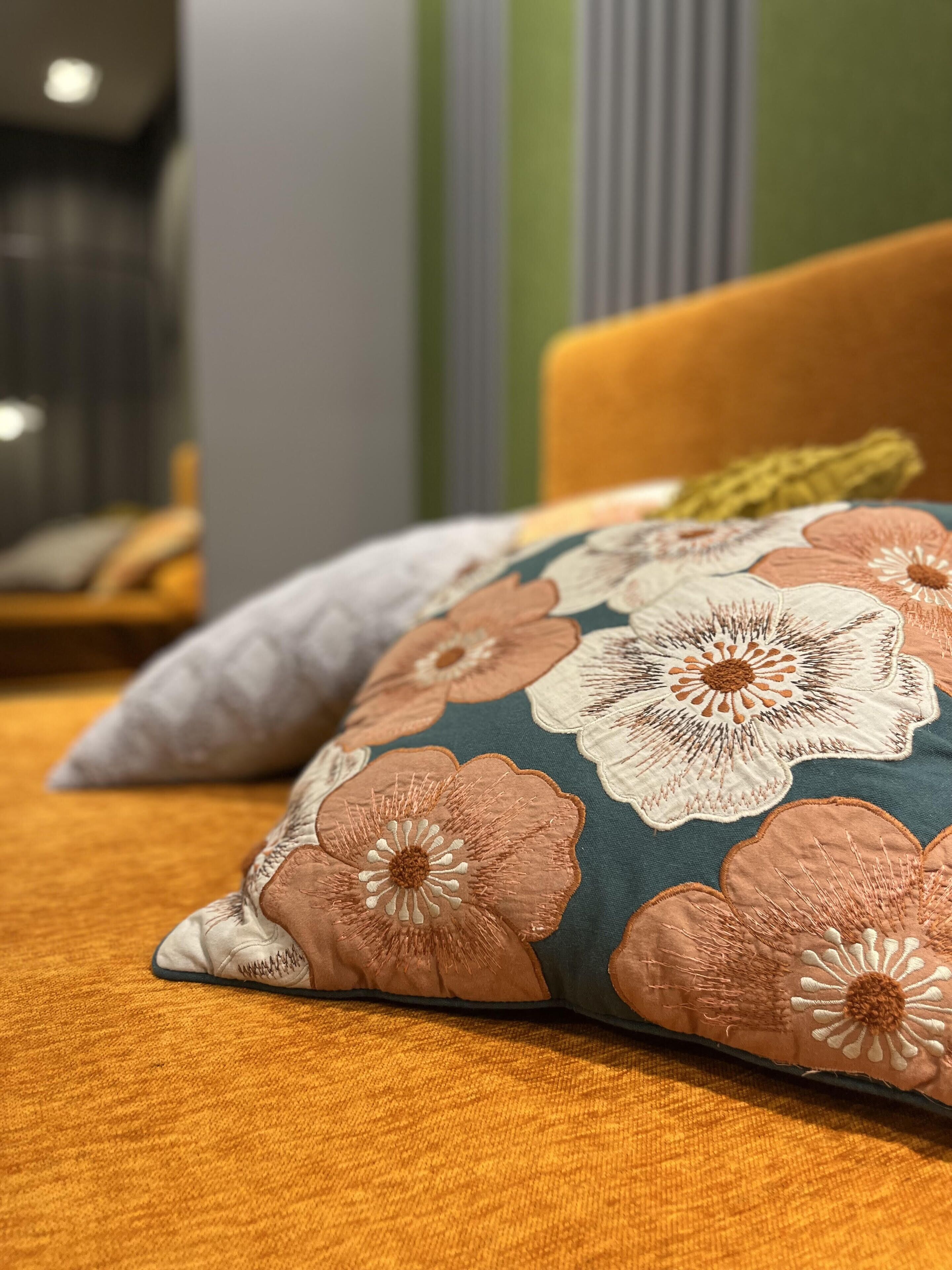 Ein Bett mit einem floralen Kissen und einem schlichten Kissen auf einer senfgelben Bettdecke.