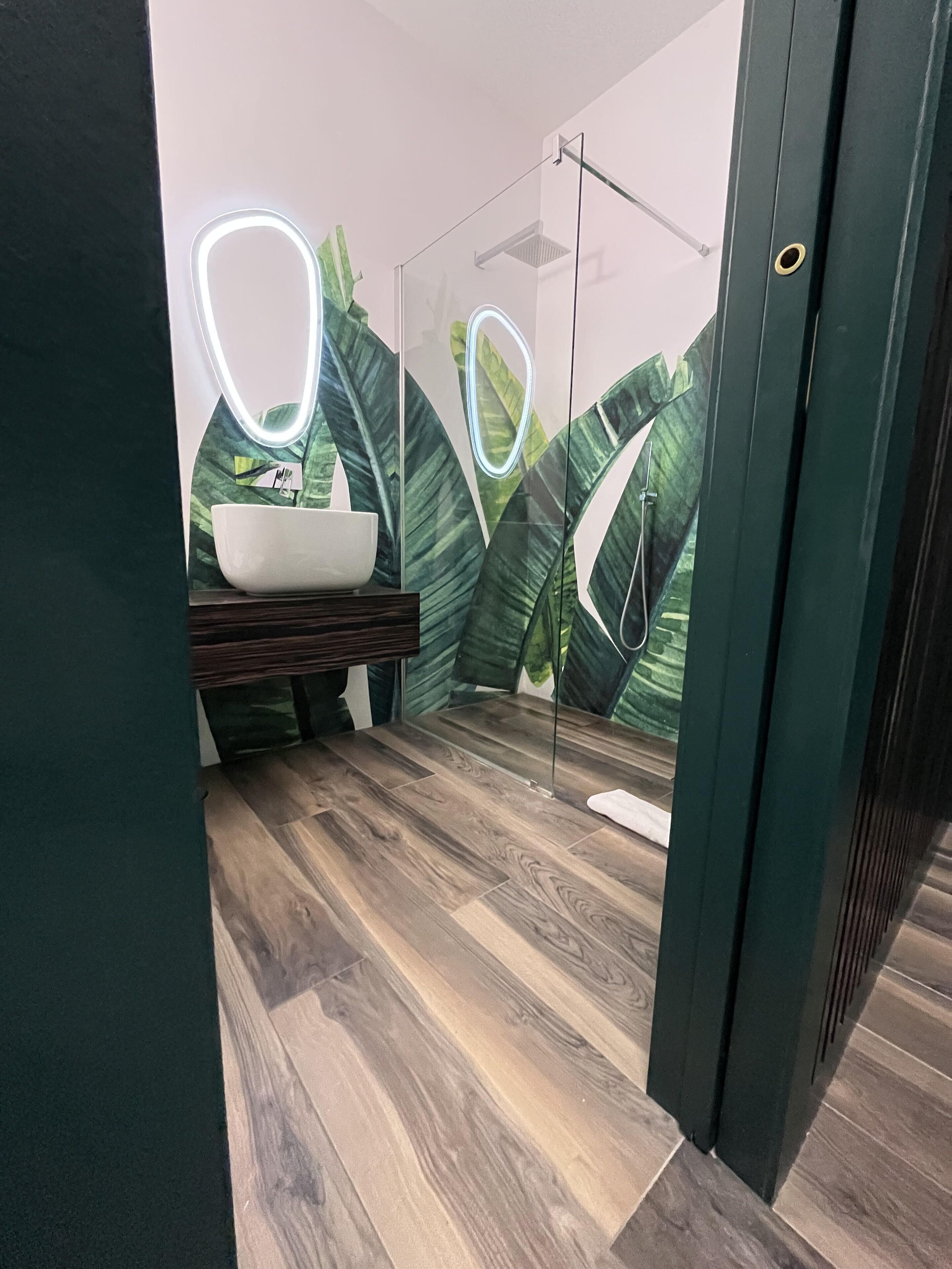 Un baño con piso de madera, un lavamanos blanco y un espejo con luces de neón.