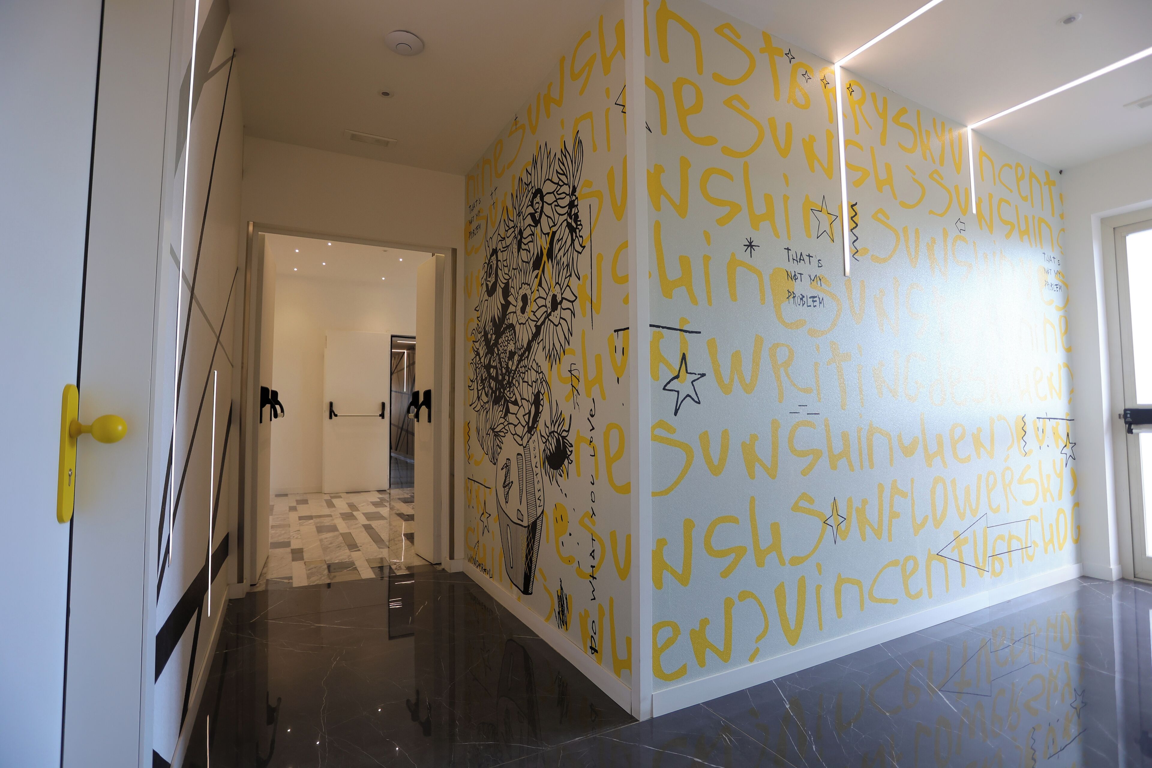 Un pasillo con suelo estampado y pared decorada con texto e ilustraciones repetidas.