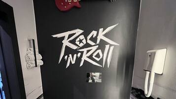 A bathroom with a black wall featuring the text "Rock 'n' Roll" and a red electric guitar. There are two sinks and a toilet.