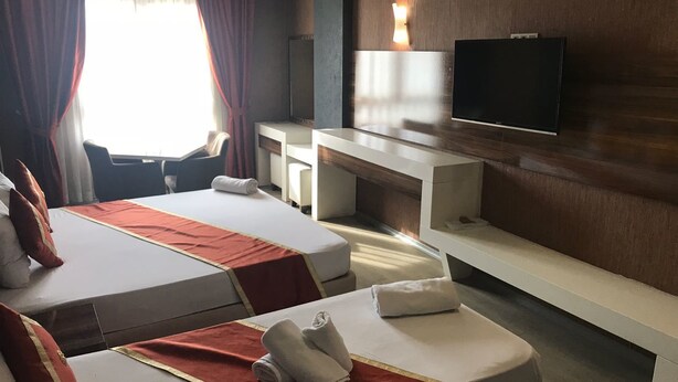 A hotel room with two beds, a desk, a chair, a TV, and a large window with curtains. - Ozcelik Hotel (Salihli)