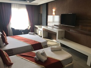 A hotel room with two beds, a desk, a chair, a TV, and a large window with curtains. - Ozcelik Hotel (Salihli)