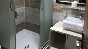 A modern bathroom with a glass-enclosed shower, a sink with a mirror, and a towel rack. - Ozcelik Hotel (Salihli)