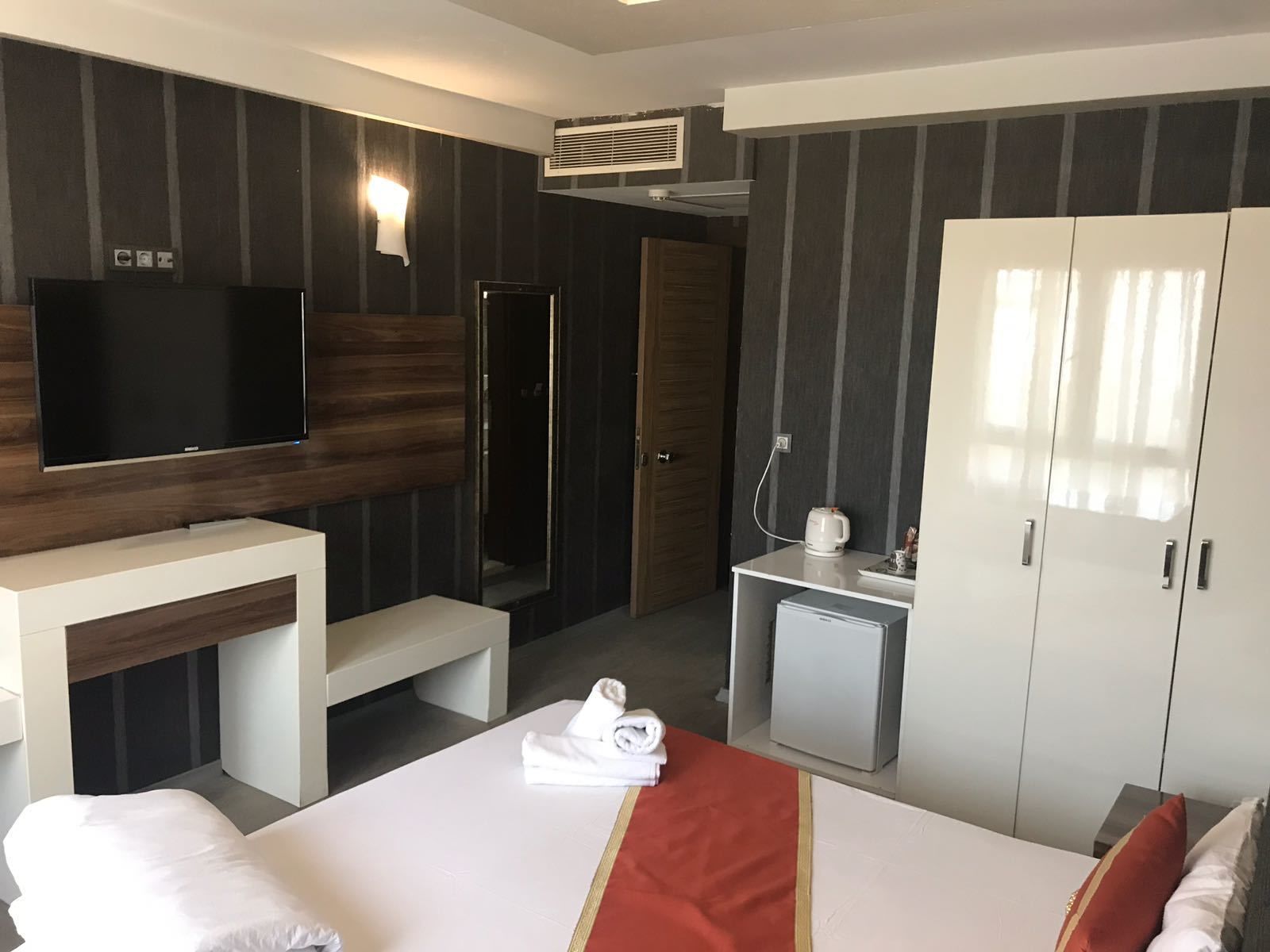 Una habitación de hotel con cama, televisión, escritorio, mini refrigerador, ducha y armario.