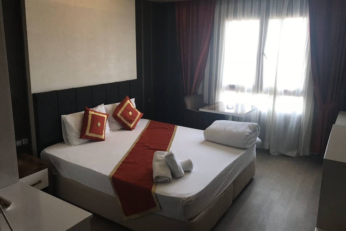 A hotel room with a large bed, a desk, and a window with curtains.