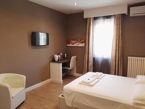 Une chambre d  ’hôtel équipée d’un lit, d’un bureau, d’une chaise, d’une télévision et d’une fenêtre avec des rideaux.