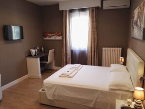 Une chambre d’hôtel équipée d’un lit, d’un bureau, d’une chaise, d’une télévision et d’une fenêtre avec des rideaux.
