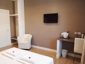 A hotel room with a bed, a chair, a TV, a small table with a kettle, and a trash bin. - Tolli Rooms (Rome)