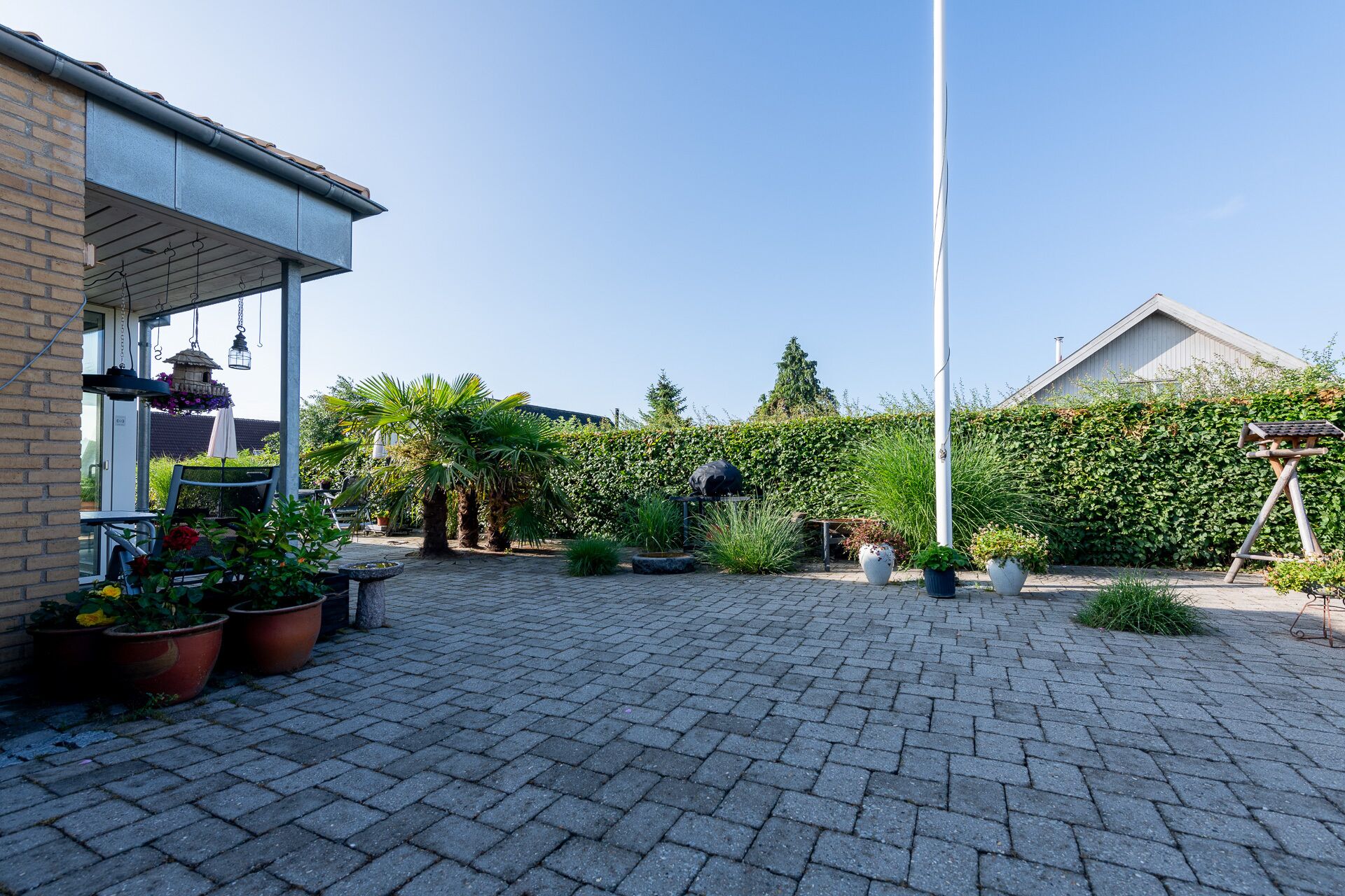 A paved courtyard with potted plants, a hanging lantern, and a metal structure.