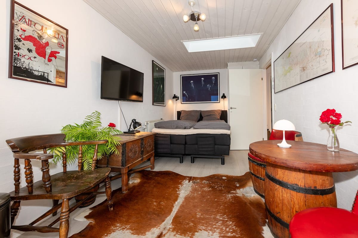 Een kleine slaapkamer met een bed, een bureau, een stoel, een kuitenvachttapijt, een houten vat en een kaart aan de muur.
