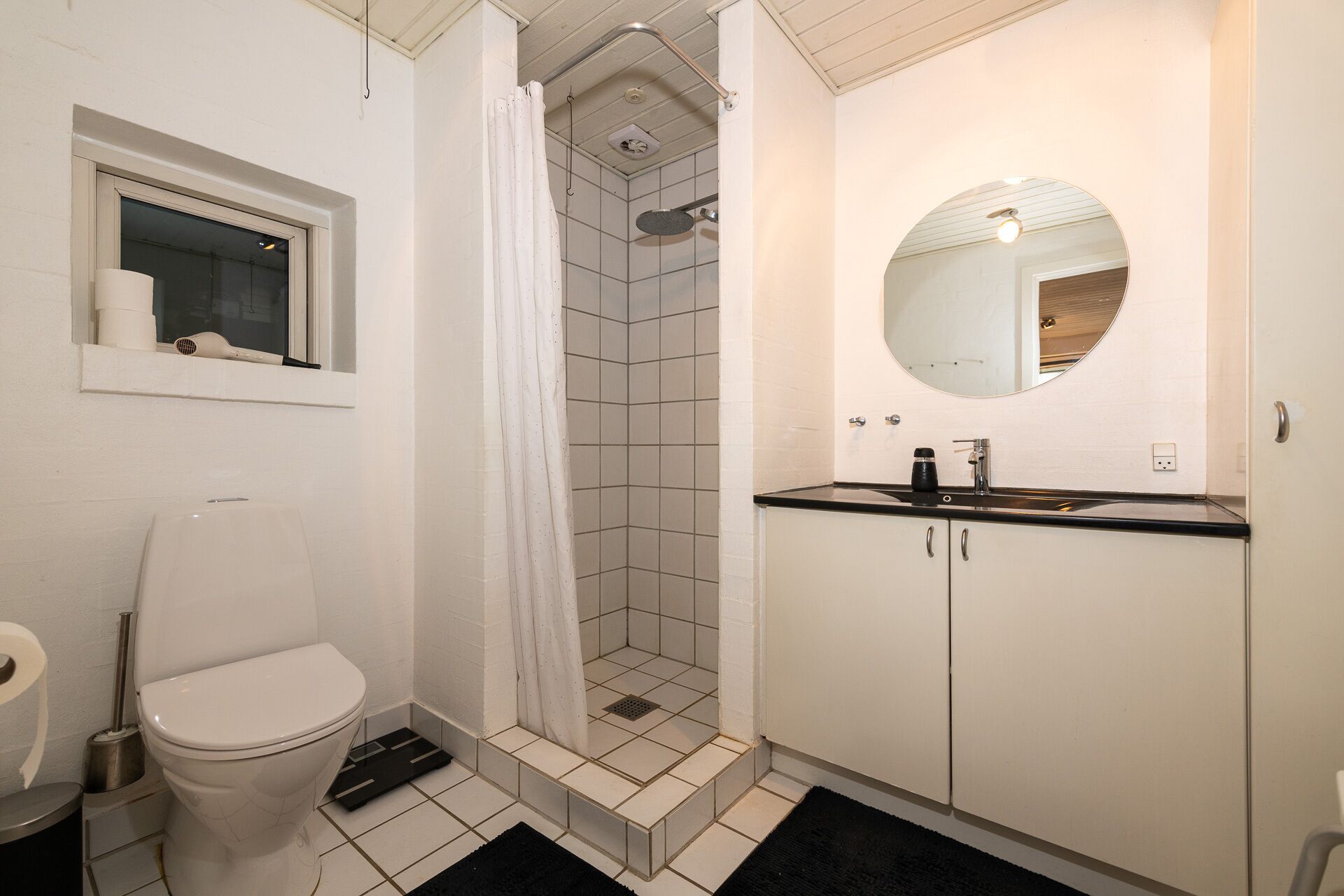 Un bagno con il water, una doccia con porta in vetro, un lavandino con specchio e una finestra con un asciugacapelli sul davanzale.