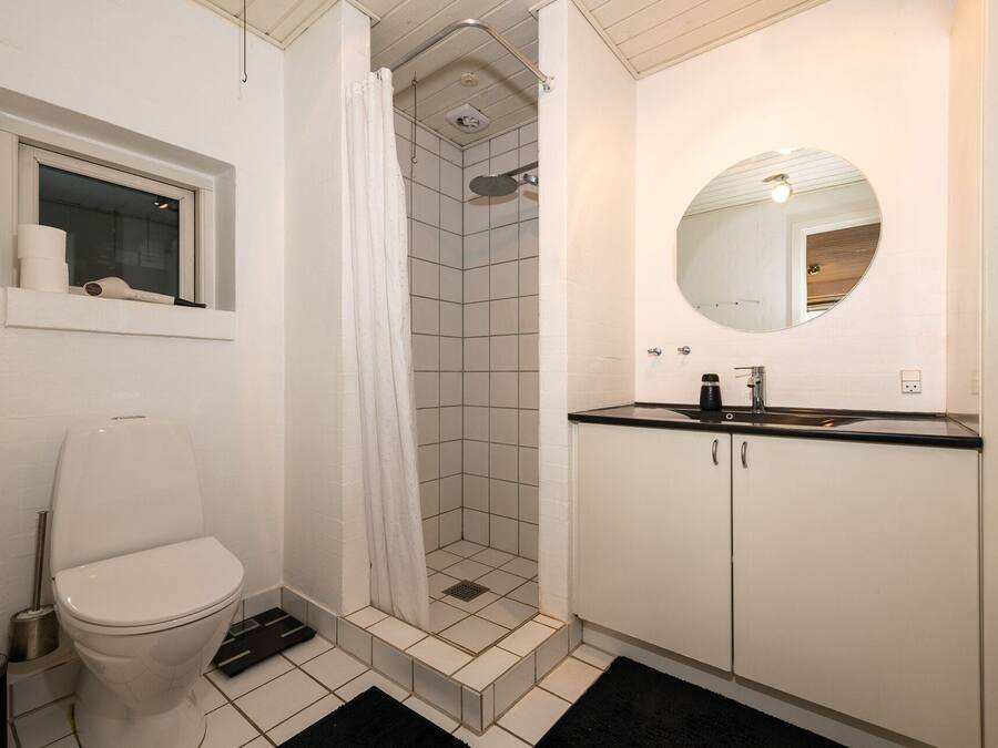 Un baño con inodoro, ducha con puerta de vidrio, lavabo con espejo y ventana con secador de pelo en el alféizar.