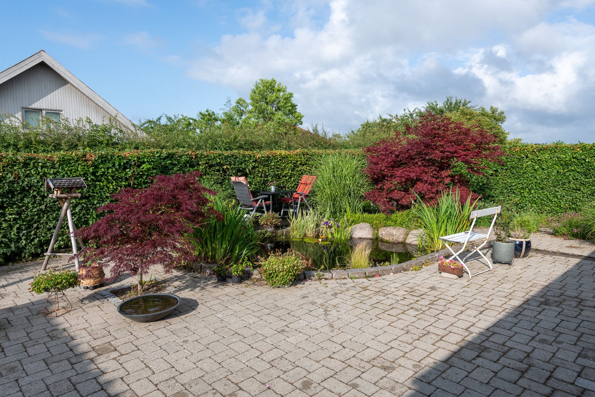 A garden with a pond, potted plants, and outdoor seating.