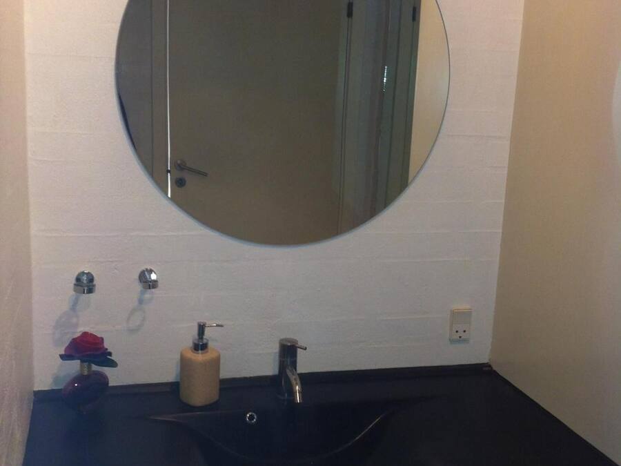 Un baño con un espejo redondo, un lavabo negro y una pared de azulejos blancos.