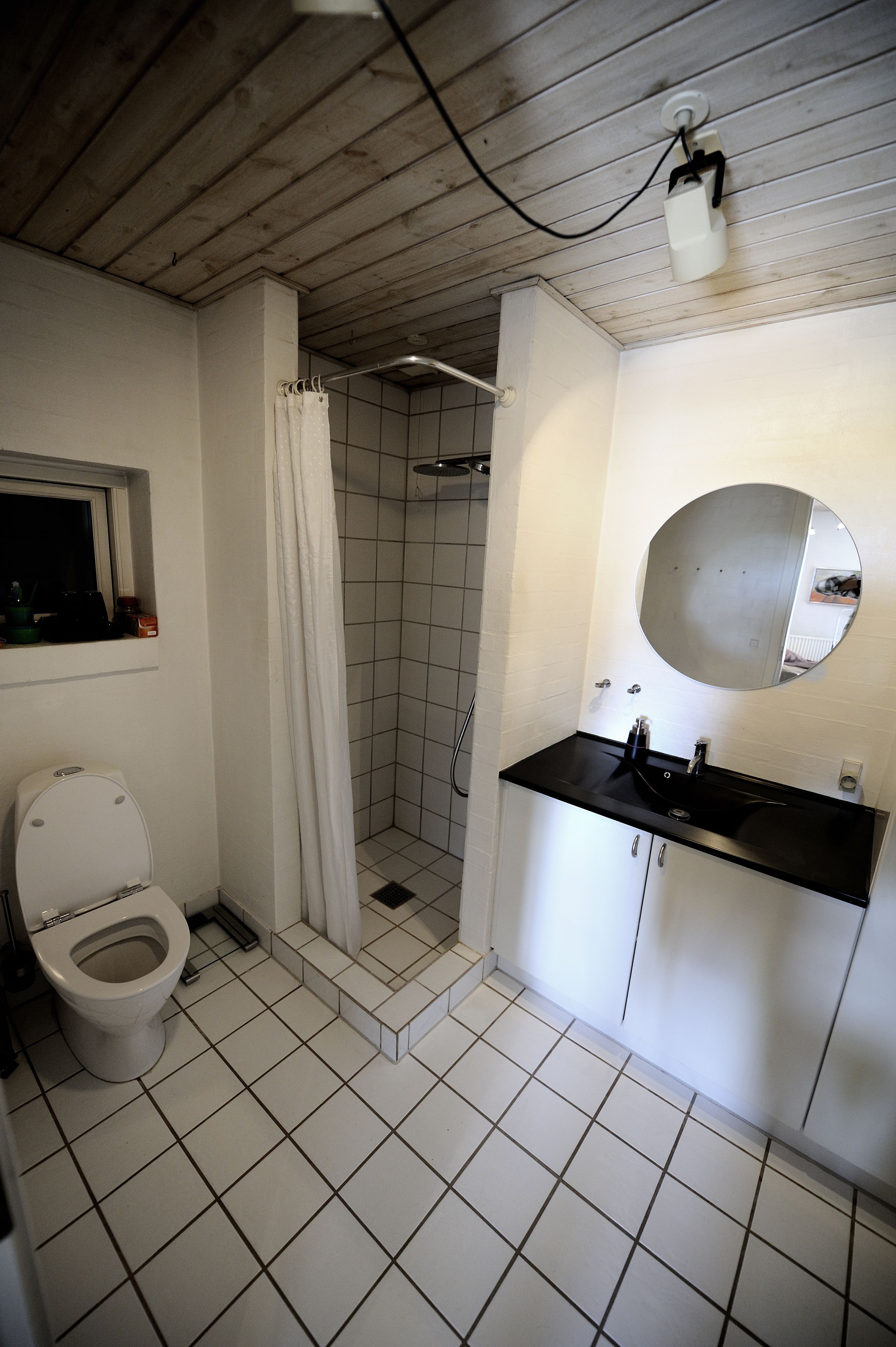 A bathroom with a toilet, a shower, a sink with a mirror, and a window above the toilet.
