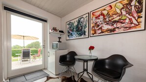Una habitación moderna con puerta de vidrio que da a un espacio exterior, dos sillas negras, una mesa pequeña con un florero y dos cuadros abstractos en la pared.