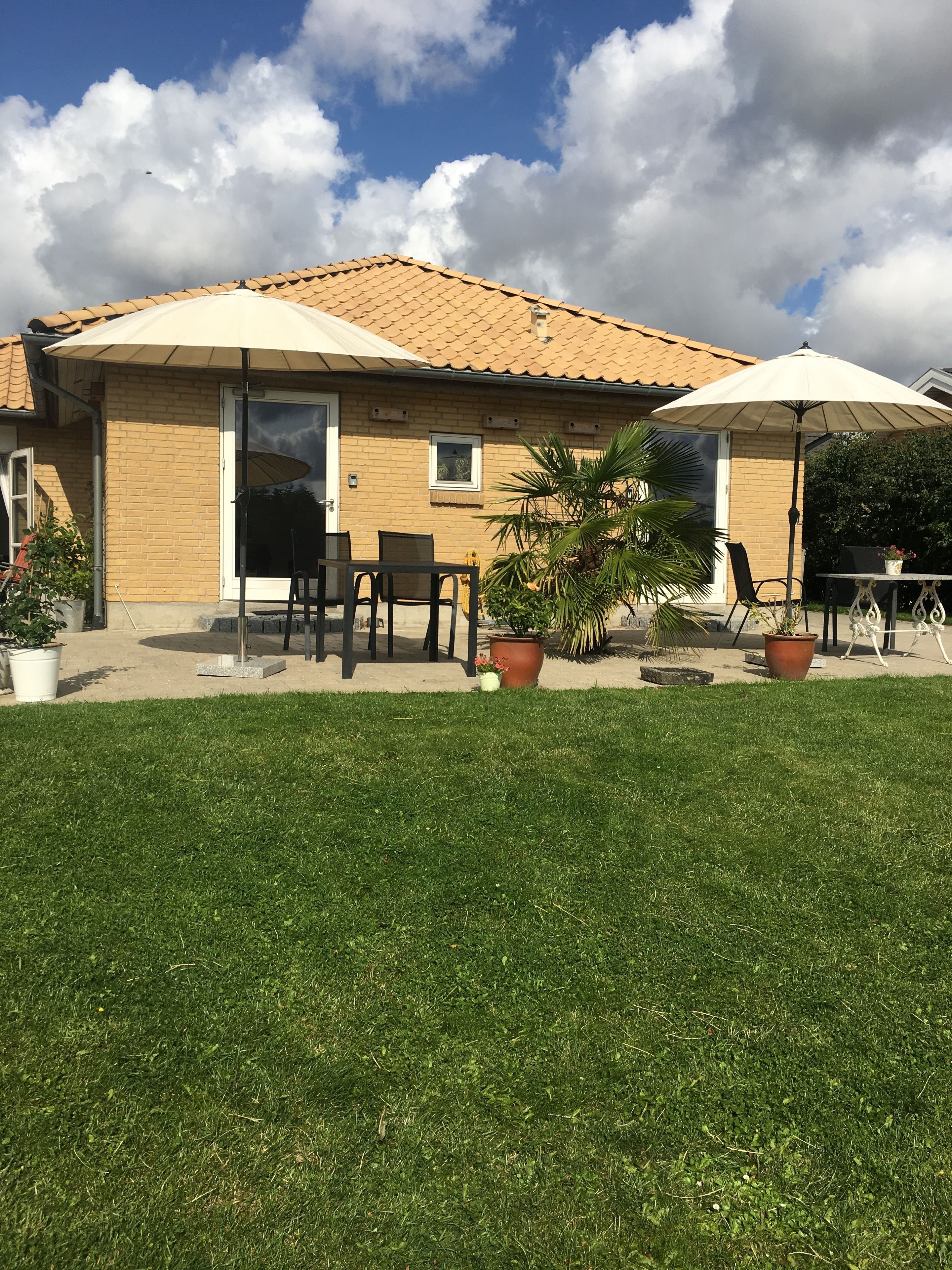 Ein Haus mit Ziegeldach, einer Terrasse mit Gartenmöbeln und einem Rasen.
