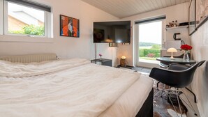 Un dormitorio con cama, escritorio con lámpara, silla, radiador y ventana con vistas a la vegetación.