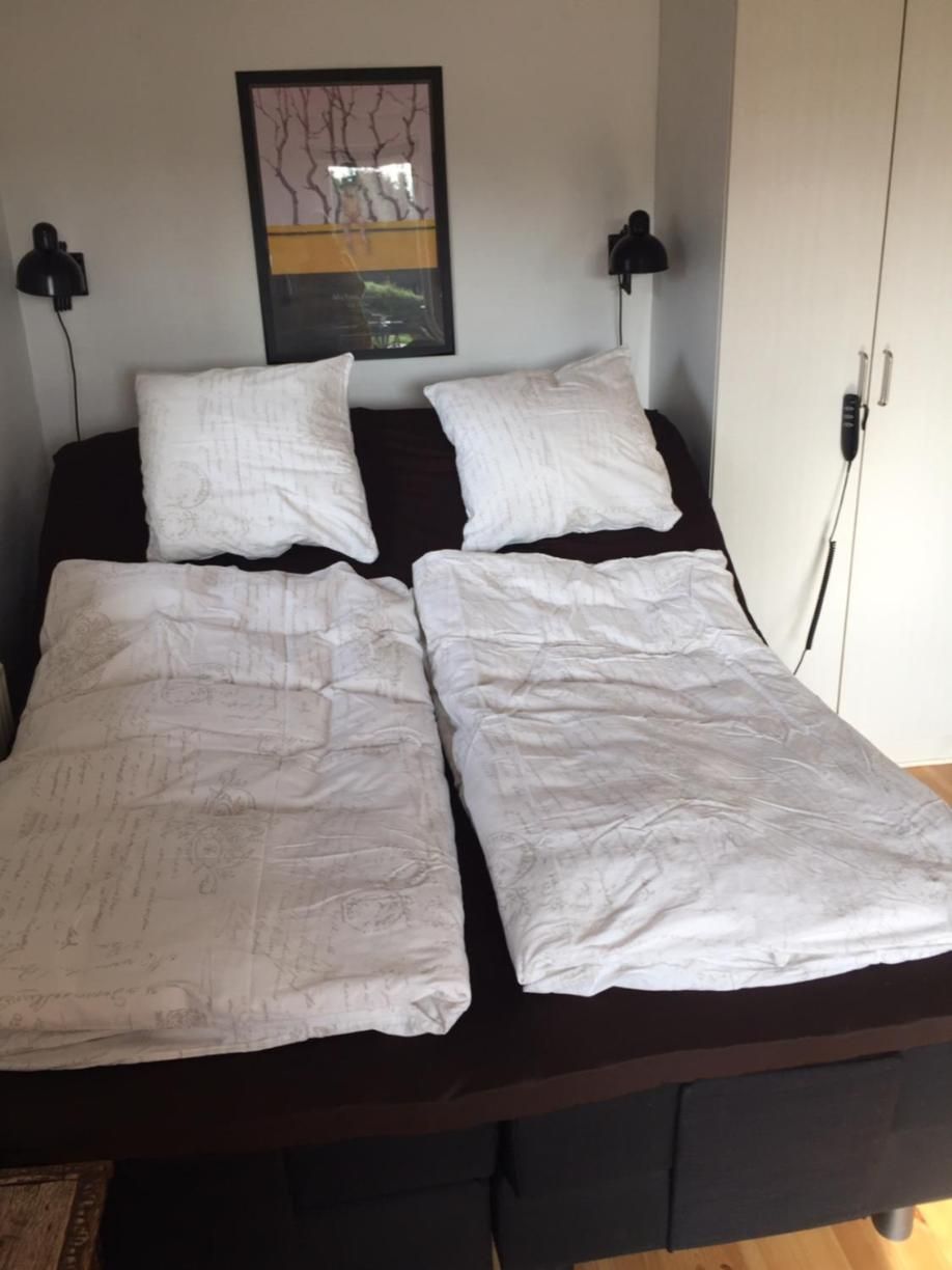 Ein Bett mit dunklem Kopfteil, zwei Nachttischlampen und einem Wandbild.