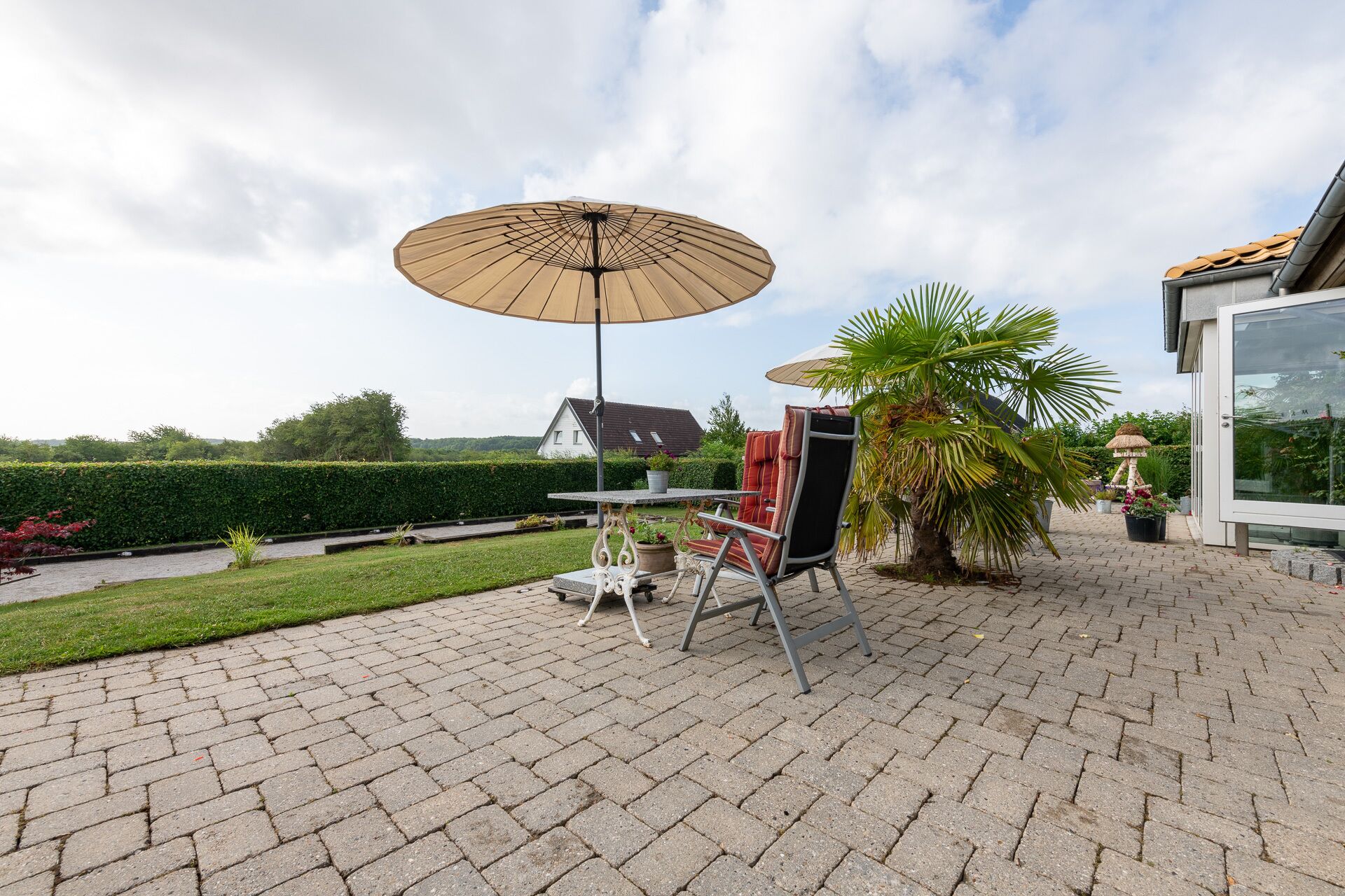 Une terrasse avec une table et des chaises, un grand parasol et un palmier.