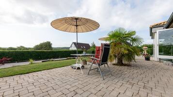 Une terrasse avec une table et des chaises, un grand parasol et un palmier.