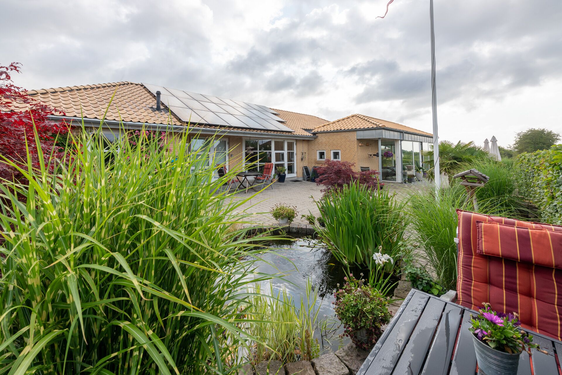 A house with a tiled roof, a small pond, and surrounding greenery.