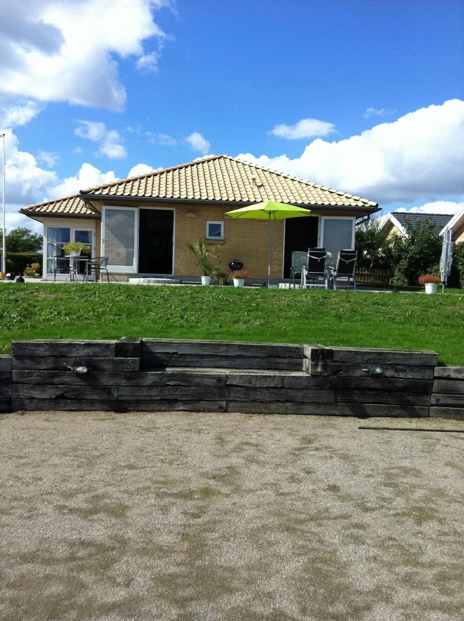 Una casa de dos pisos con techo de tejas, un patio con mobiliario exterior y una sombrilla verde.