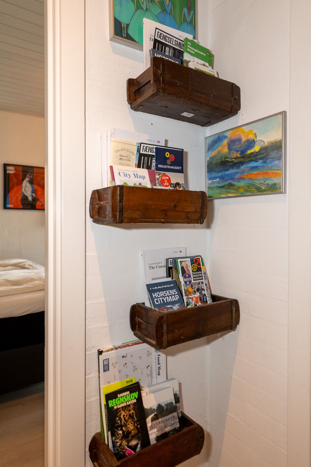 Una pared con estantes de madera que sostienen varios libros y un cuadro.