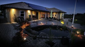 Una casa con panel solar, estanque y mobiliario exterior.