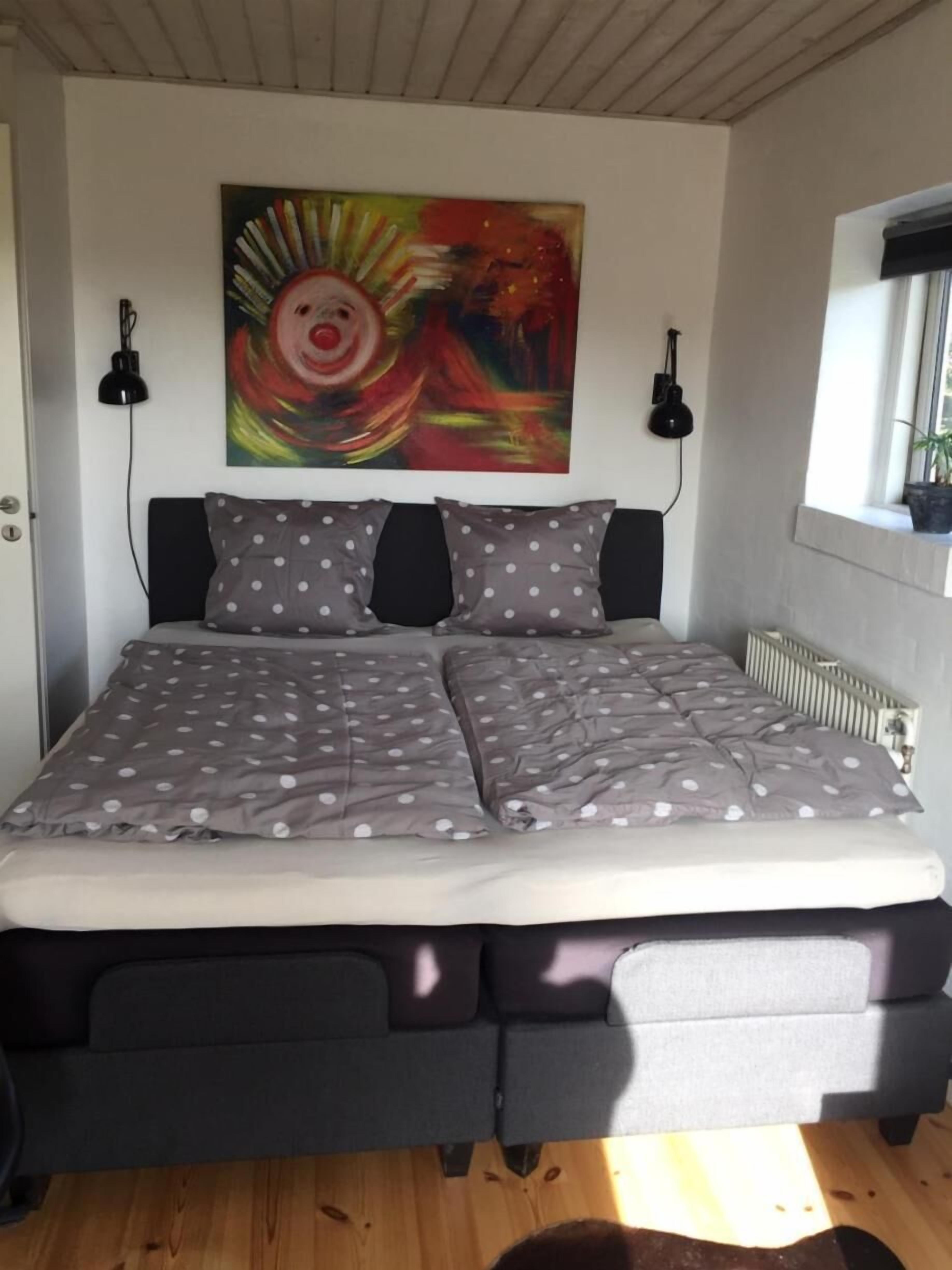 A bed with a polka dot bedspread, two black wall-mounted lamps, and a colorful abstract painting above the bed.