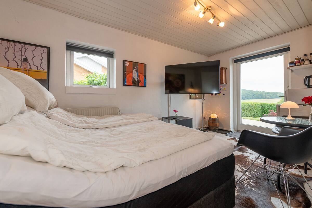Een slaapkamer met een groot bed, een flatscreen televisie aan de muur, een tafeltje met een lamp en een stoel.
