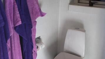 Un baño con un inodoro, una ventana encima y un perchero con toallas moradas.