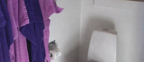 Un baño con un inodoro, una ventana encima y un perchero con toallas moradas.