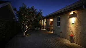 Una casa de ladrillo con un camino pavimentado, un árbol pequeño y una pared exterior bien iluminada.
