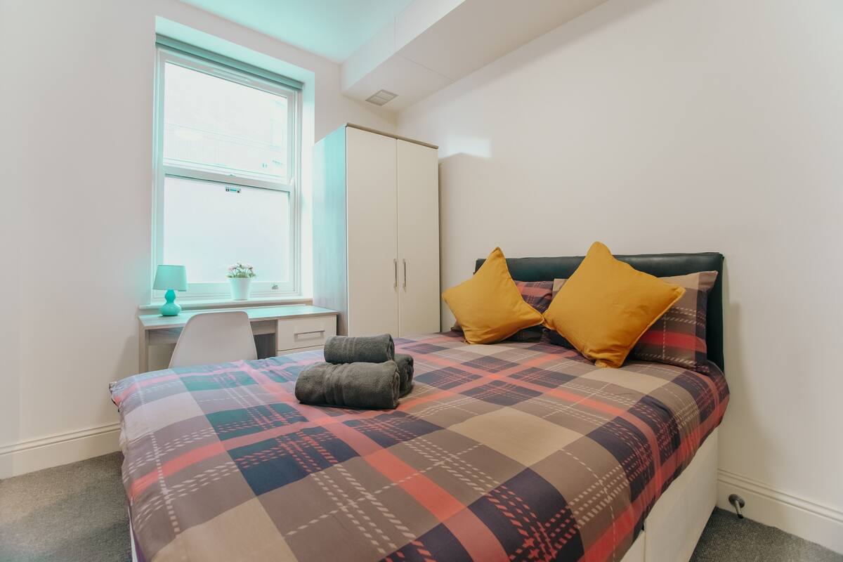 Um quarto com uma cama, uma escrivaninha e uma janela.