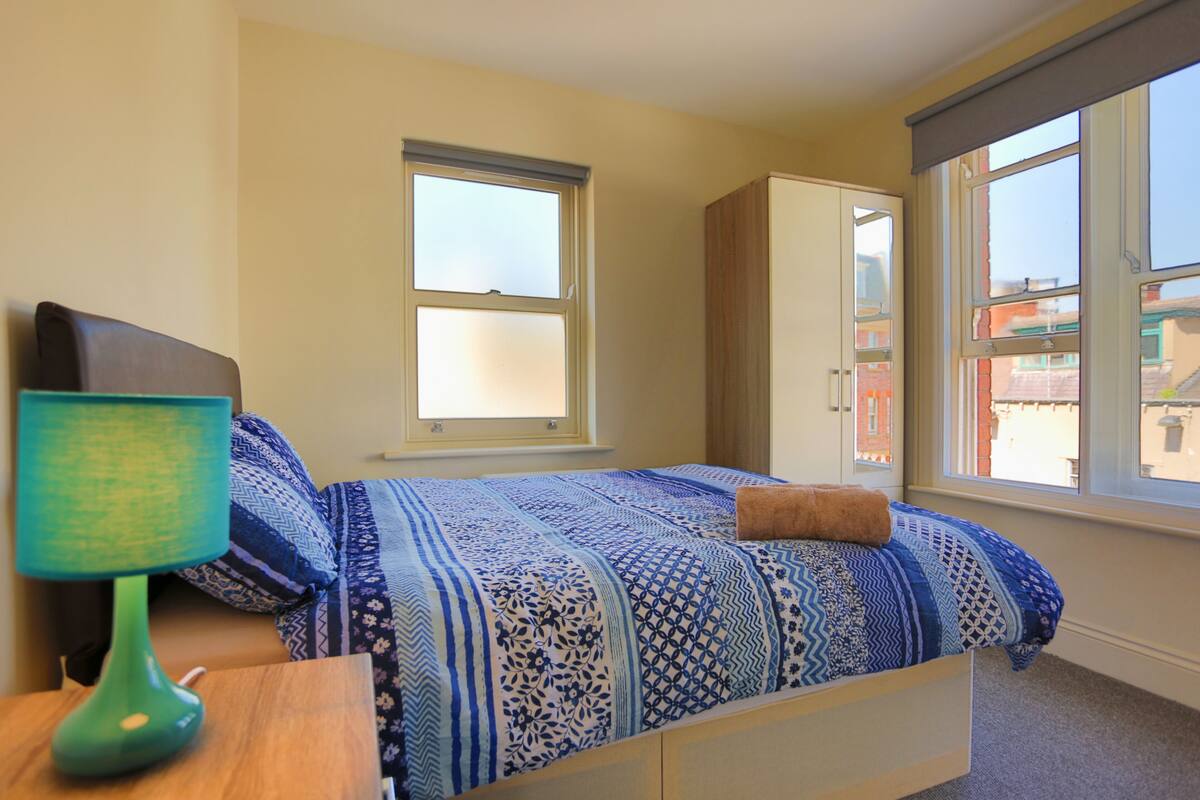 Quarto com uma cama, mesa de cabeceira, abajur e janela.