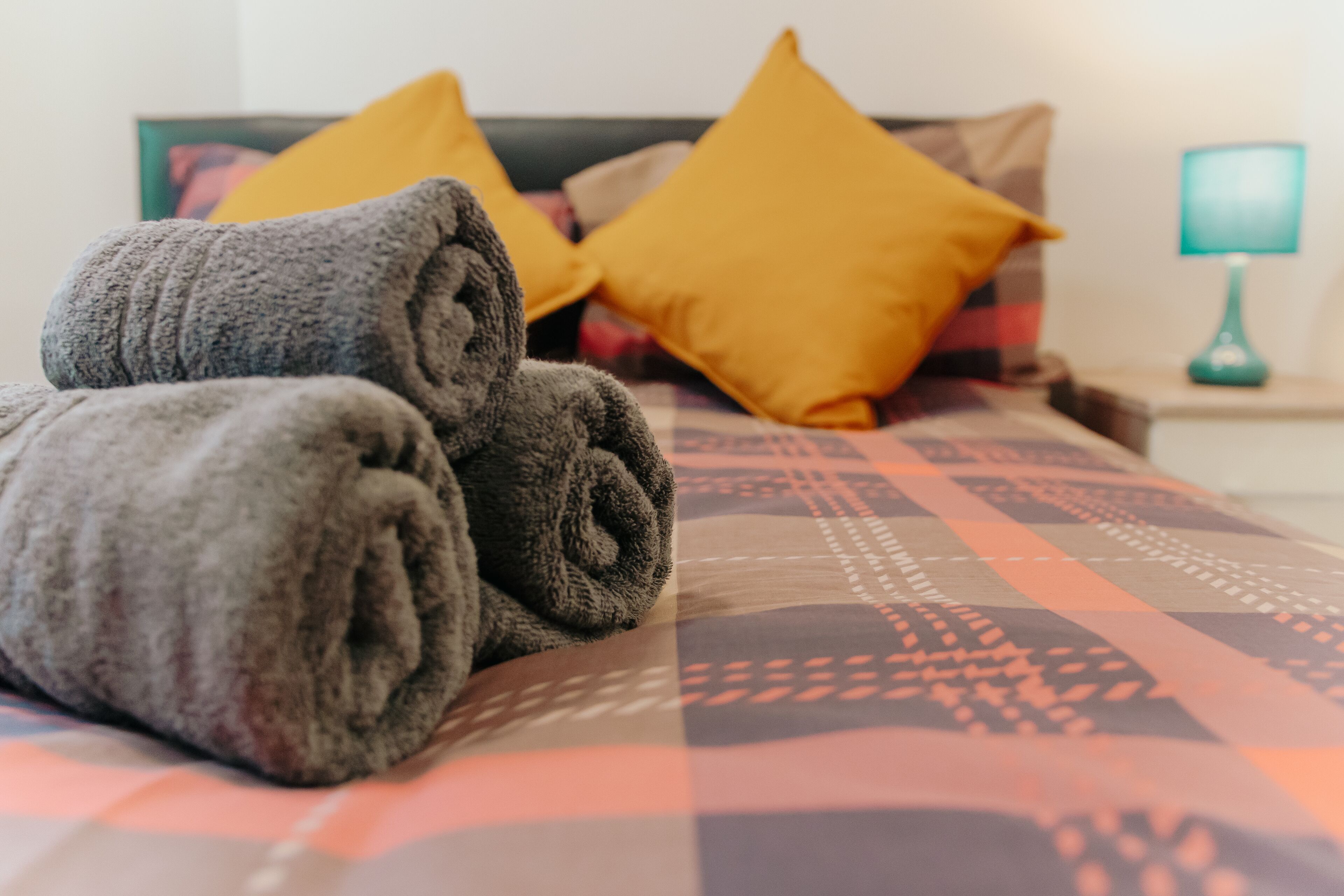 A neatly made bed with rolled towels and patterned bedding.