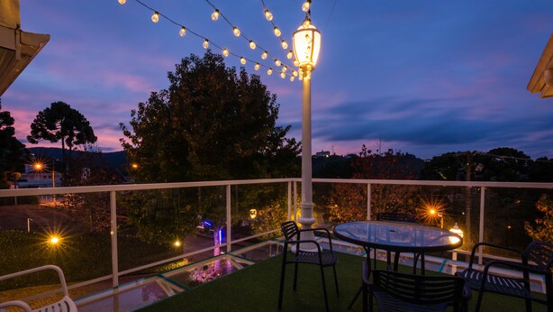 An outdoor patio with a round table and chairs, surrounded by a white railing, and string lights overhead.