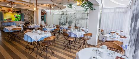 A restaurant with multiple tables set for dining, featuring white tablecloths and metal chairs.