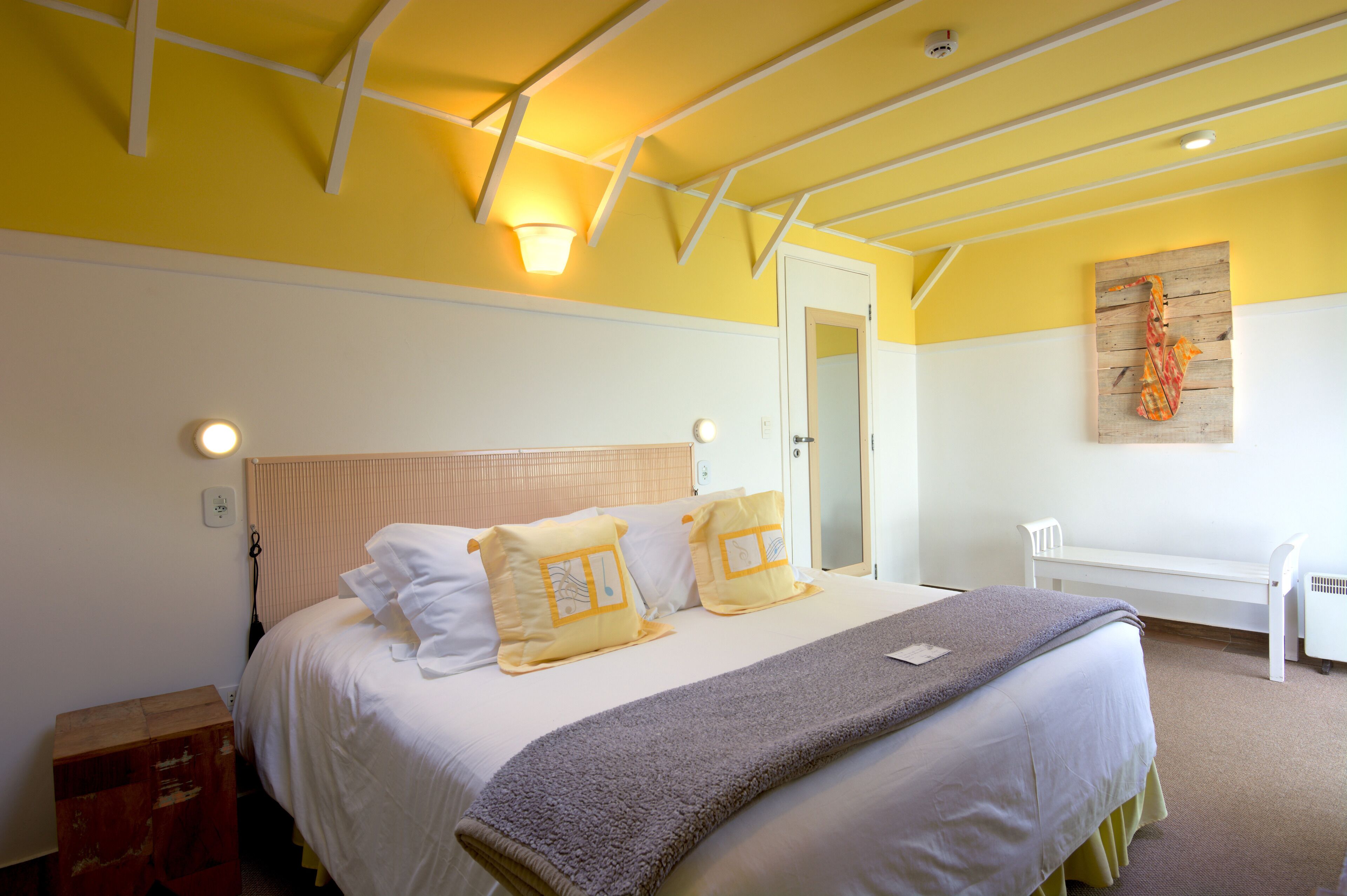 A hotel room with a bed, bedside table, and a bench.