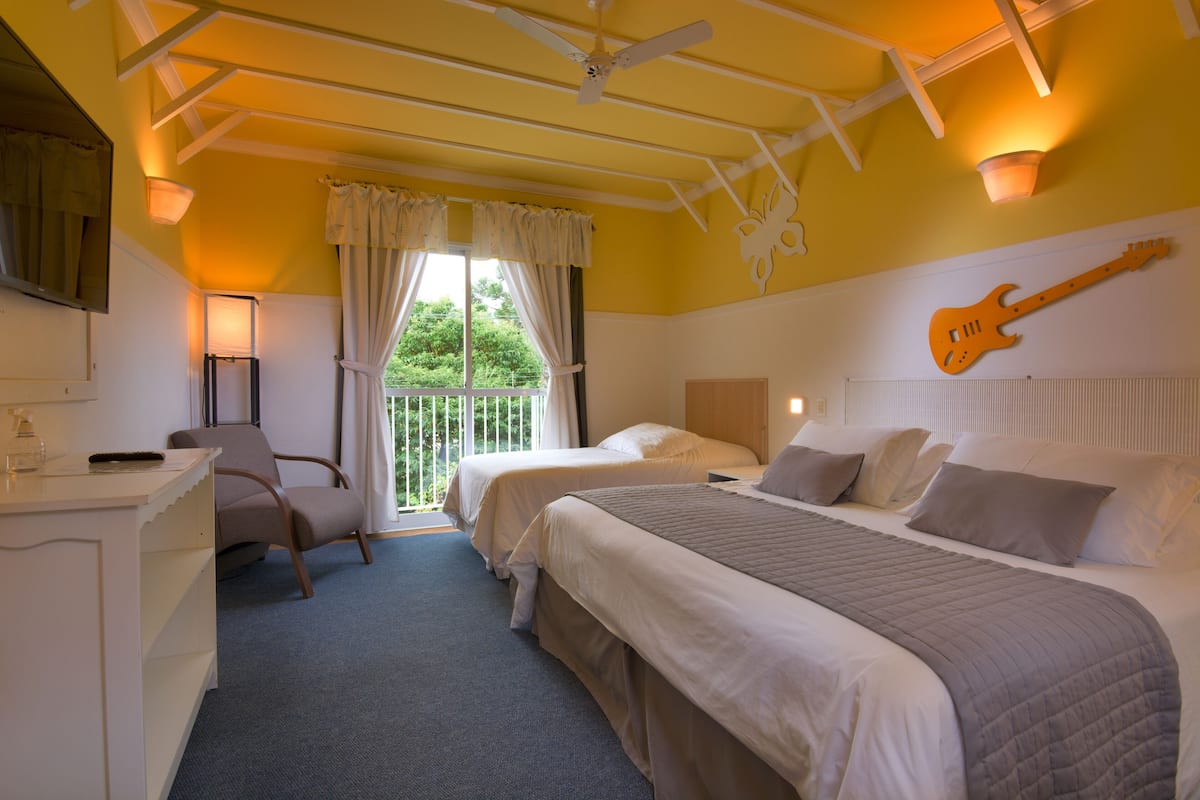 Een hotelkamer met twee bedden, een bureau, een stoel en een gitaar aan de muur.