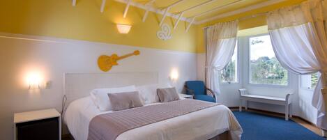 A bedroom with a bed, a guitar wall decoration, a bench by the window, and a ceiling fan.