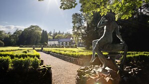 Una estatua en un jardín con un camino que conduce a un edificio.